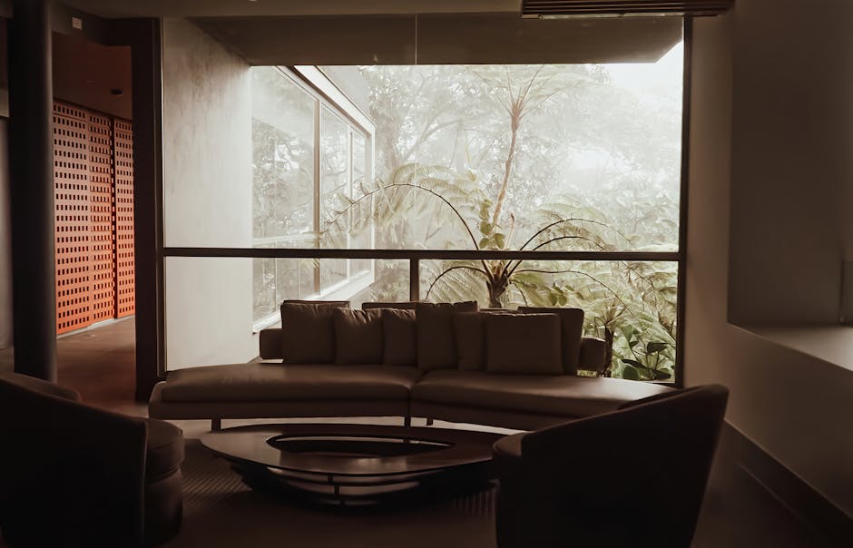 Modern living room interior featuring large windows and lush jungle view.