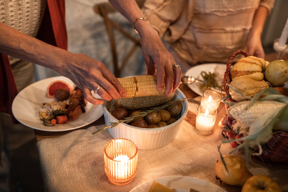 A warm Thanksgiving dinner setting with hands serving corn and vegetables, lit by candlelight.