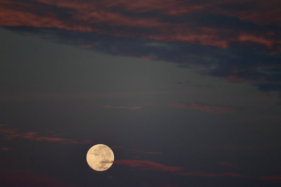 A tranquil view of a full moon against a dramatic cloudy sky at night.