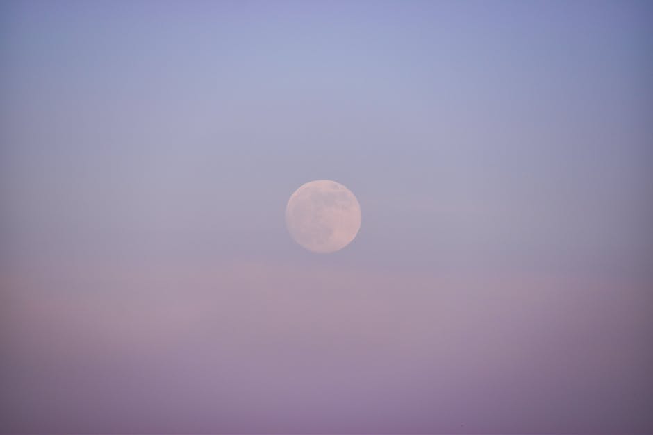 Serene view of the full moon enveloped in a soft, foggy twilight sky creating a mystical atmosphere.