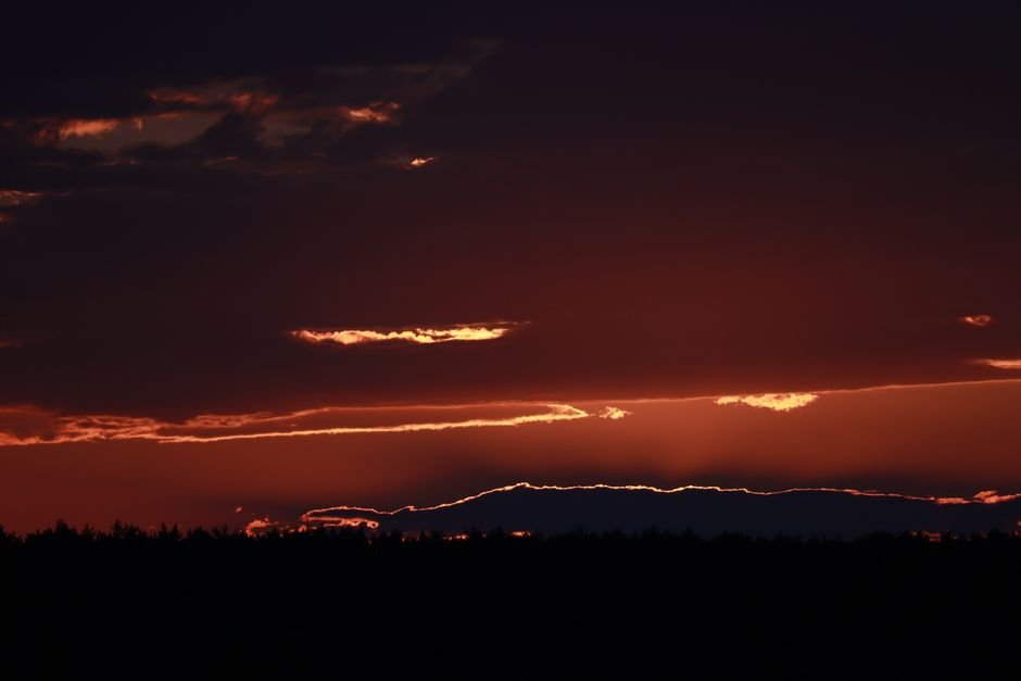 A breathtaking sunset casting silhouettes over distant trees, creating a dramatic and serene scene.