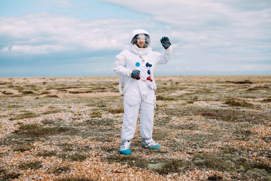 Astronaut in a spacesuit waving in an open desolate landscape under a cloudy sky.