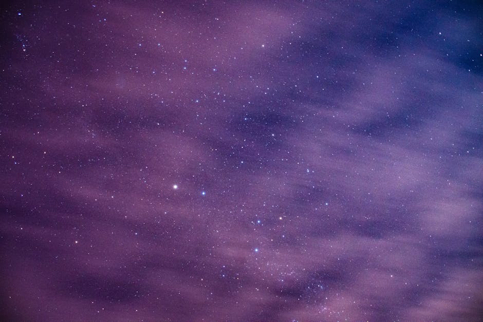 Long exposure of cosmic background with dark night sky with glowing bright stars behind light floating clouds