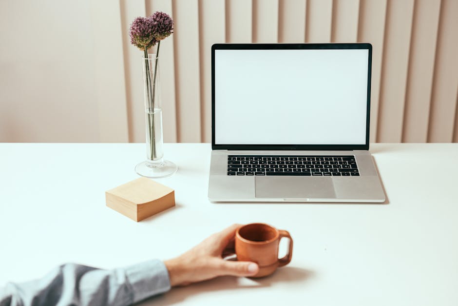 A minimalist workspace setup featuring a laptop, coffee mug, and decorative vase with flowers.