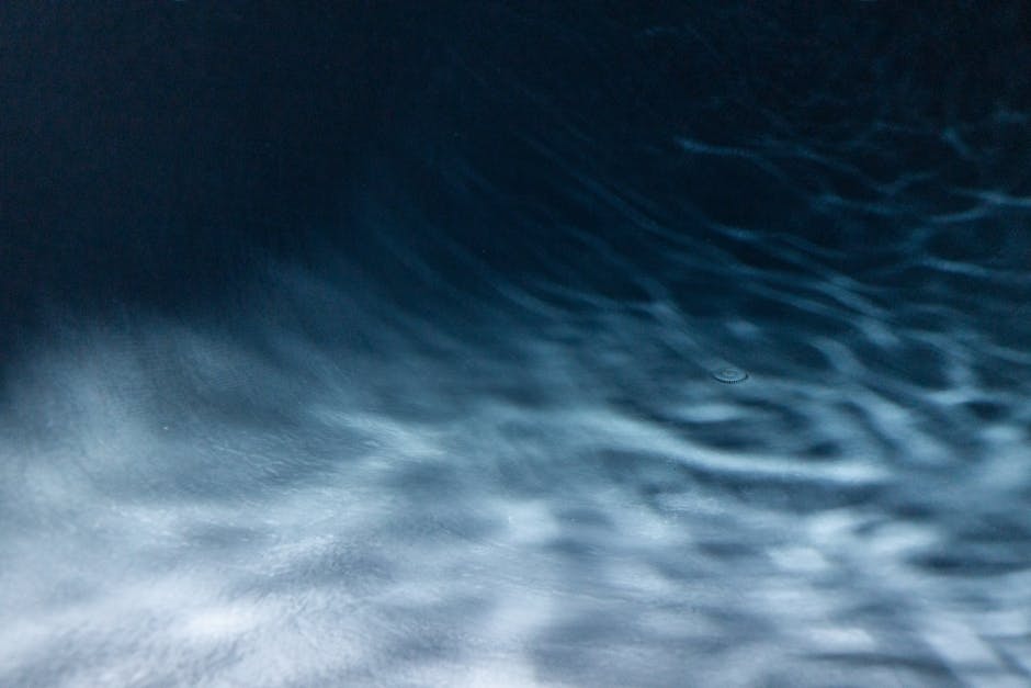 A close-up abstract view of a rippling water surface with dark blue hues and light reflections.