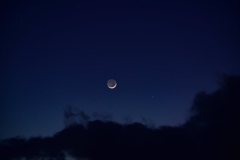 A serene crescent moon surrounded by deep blue night sky and fluffy clouds.