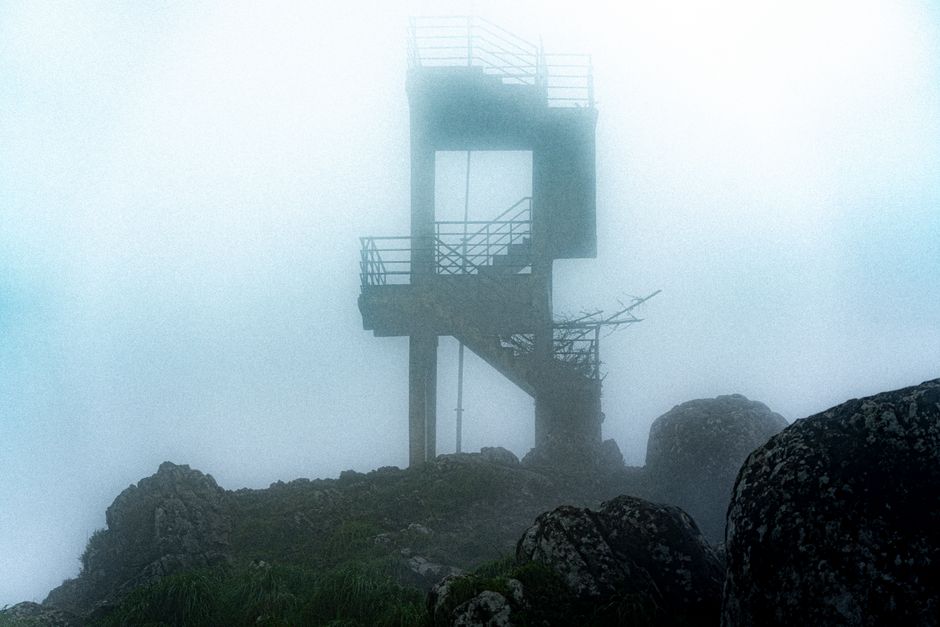 Eerie tower shrouded in mist amid rocky landscape in Ponmudi, India.