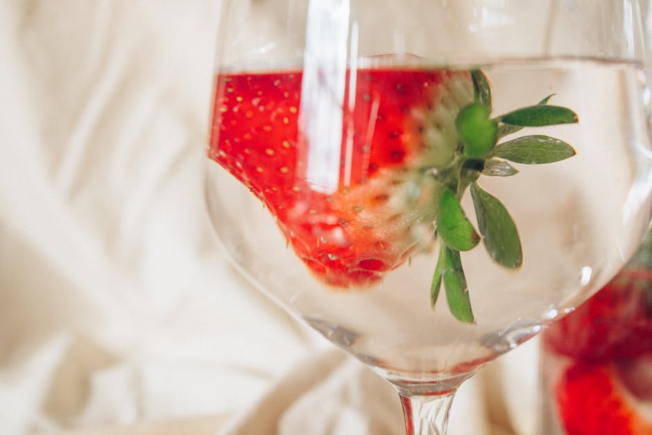 A close-up of a strawberry submerged in a wine glass filled with water, highlighting its fresh and vibrant hues.