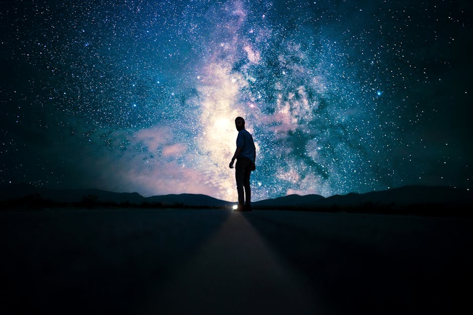 Silhouette of a man standing on a road, gazing at a stunning star-filled night sky with the Milky Way.