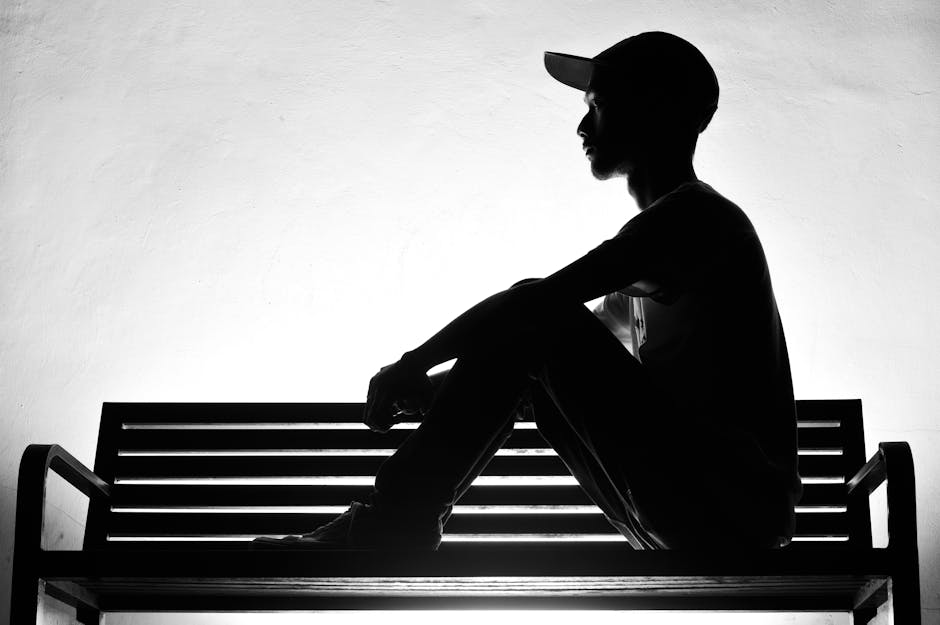 A dramatic black and white silhouette of a person sitting thoughtfully on a bench.