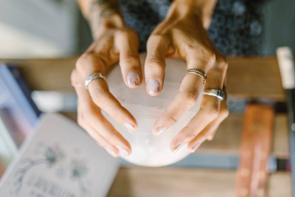 Hands wearing rings holding a crystal sphere, symbolizing spirituality and healing.